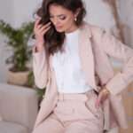 A very attractive brunet woman with a nice make up, wearing pale pink blazer, white blouse and pink trousers, all as monochromatic is touching her hair in seductive manners. Photo cover of the blogpost about: Why the Neutral Tones are the Secrets to Timeless Elegance?
